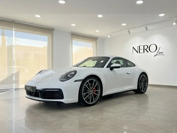 تُعرض سيارة بورش 911 كاريرا إس 992 (كوبيه) البيضاء من زاوية ثلاثة أرباع أمامية في صالة عرض مشرقة بمدريد.