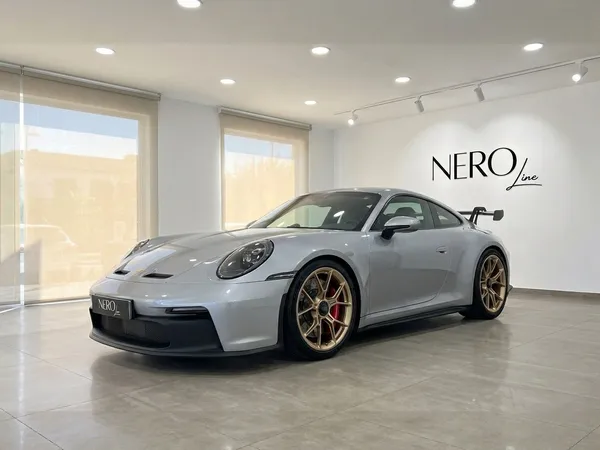 سيارة بورش 992 GT3 الفضية اللامعة معروضة من زاوية أمامية ثلاثة أرباع في صالة عرض مشرقة في إيبيزا.