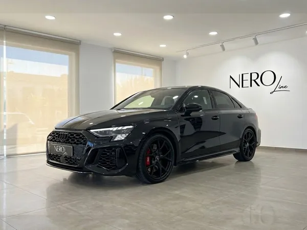 The sleek black 2022 Audi RS3 Saloon is showcased from a front three-quarter angle in a modern Marbella showroom.