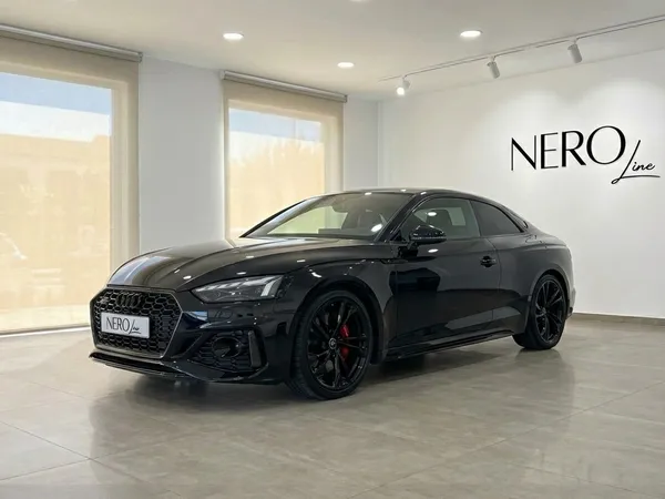 The black 2025 Audi RS5 luxury sedan is showcased from a front three-quarter view in a Marbella showroom.