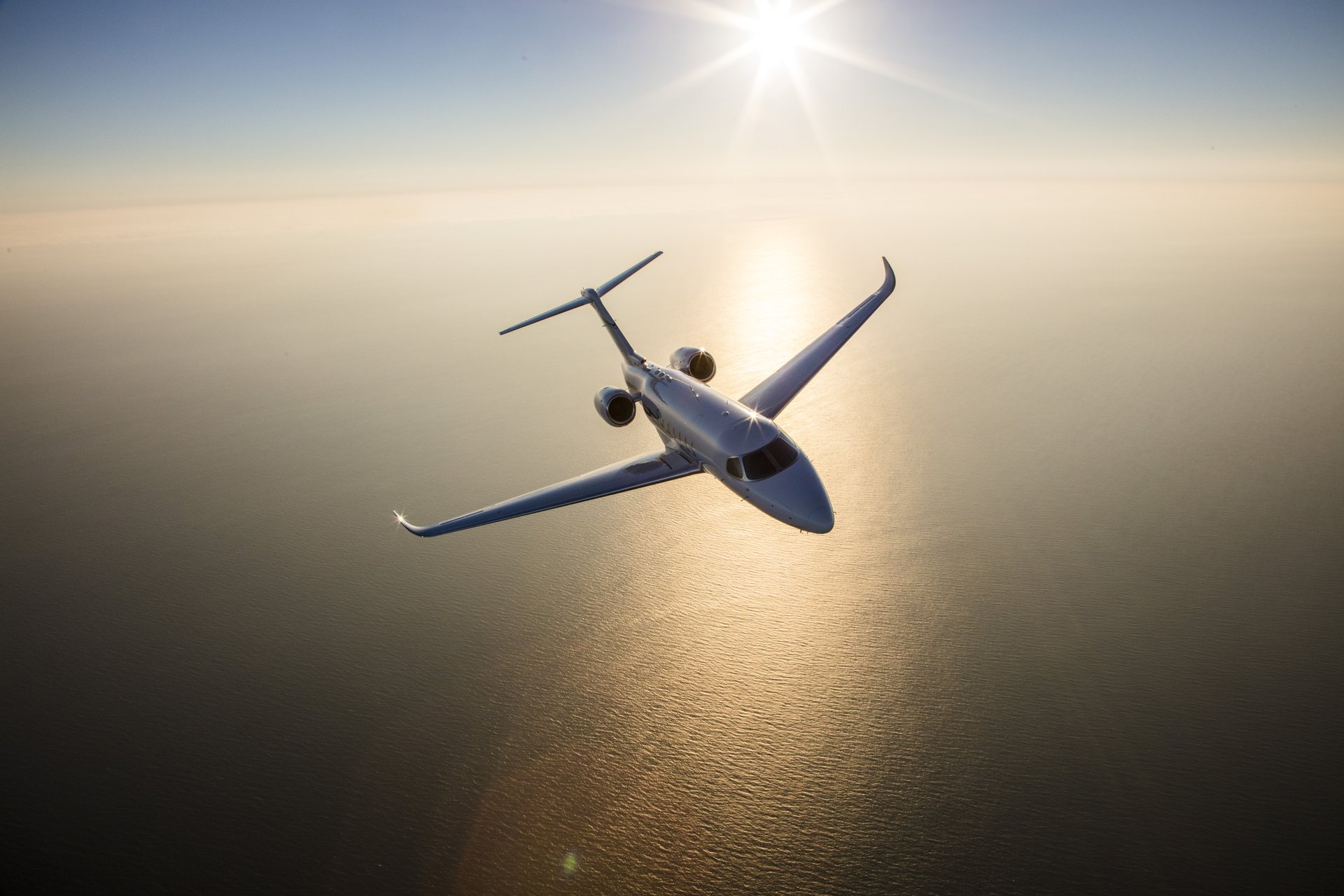 Cessna Citation Longitude — Aerial sunset flight A Cessna Citation Longitude private jet soars high above the sun-drenched ocean, reflecting the golden light of sunset.