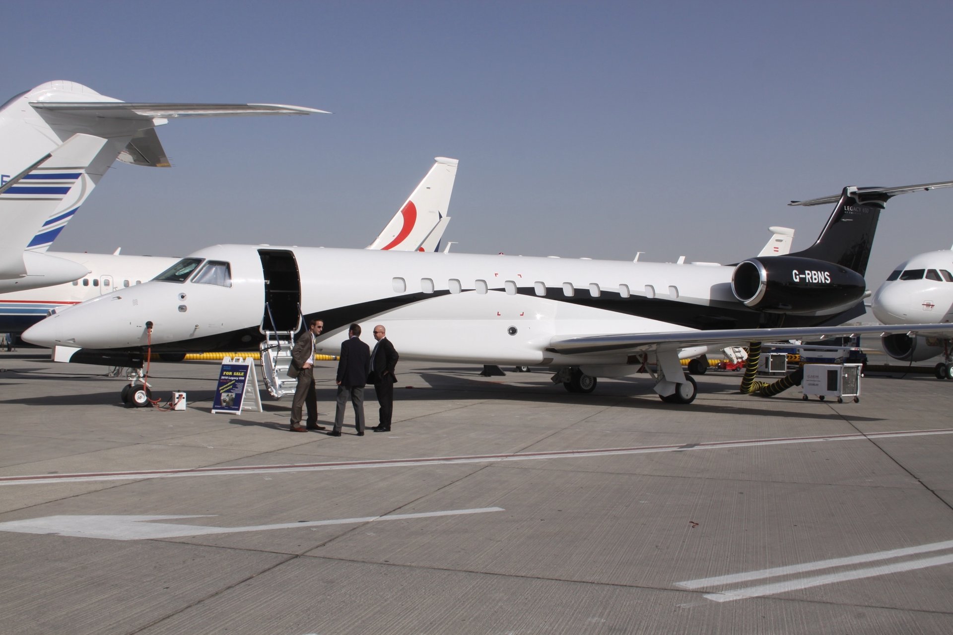 Embraer Legacy 650 — Side view on airfield The Embraer Legacy 650 private jet is seen from the side on an airfield in Ibiza, with its main door open and three men standing nearby.