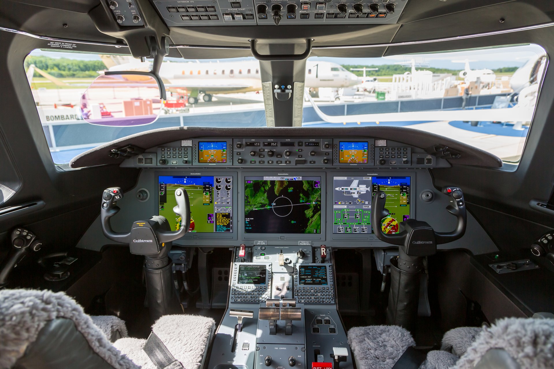 Gulfstream G280 — Advanced cockpit view The advanced cockpit of a Gulfstream G280 private jet, featuring multiple digital displays, flight controls, and a view of other aircraft on the tarmac.