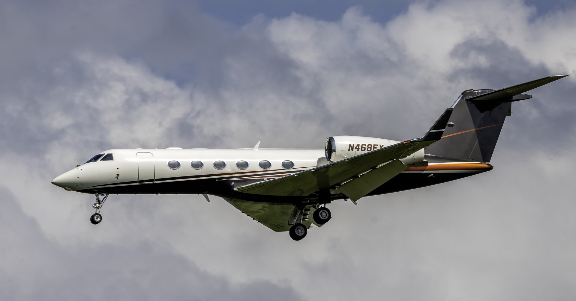 Gulfstream G450 — Private jet in flight over Madrid A white and black Gulfstream G450 private jet in flight with its landing gear extended, seen from the side against a cloudy sky over Madrid.