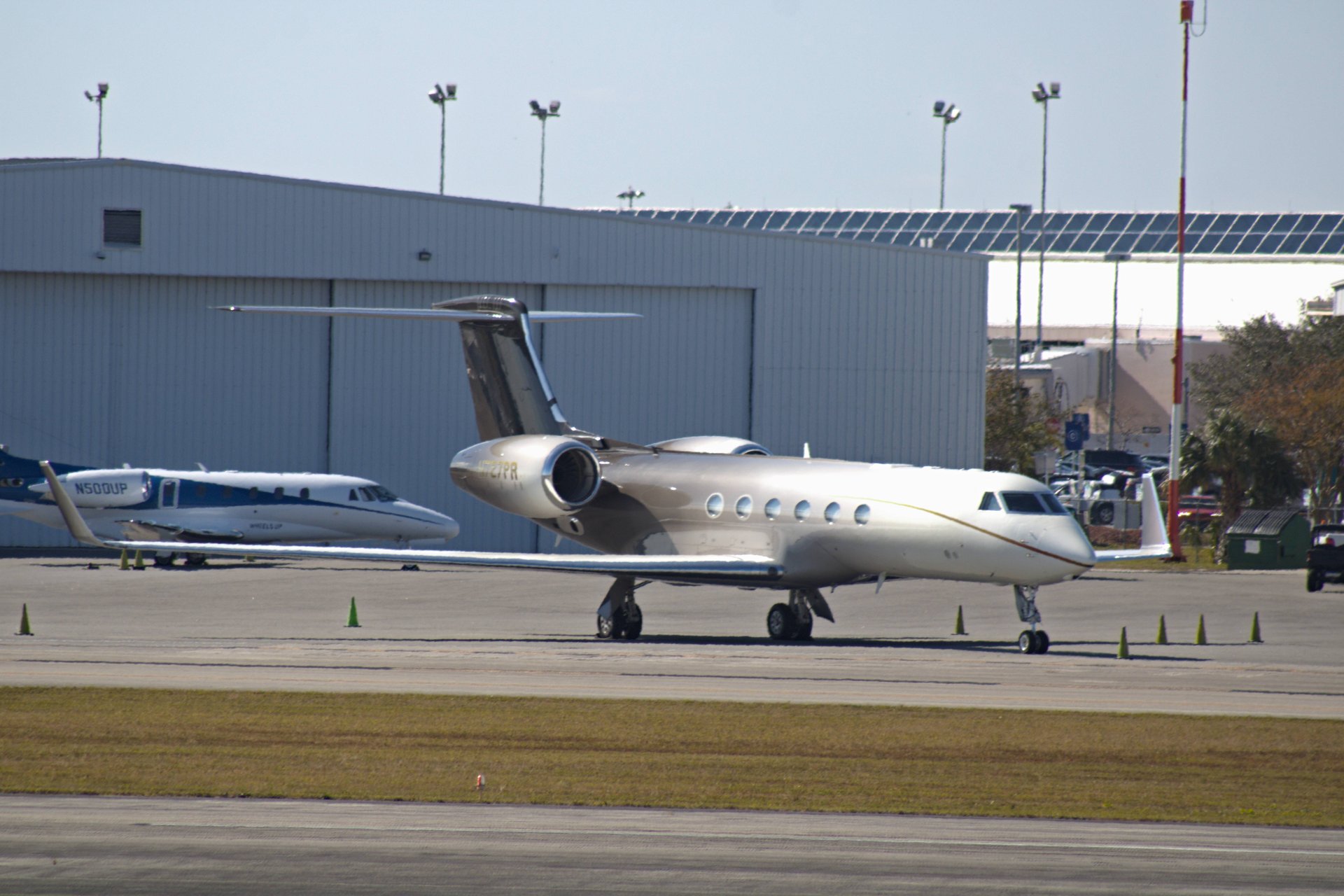 A sleek Gulfstream GV private jet is parked on the tarmac, seen from its side, with another smaller jet and a hangar in the background at an airport.