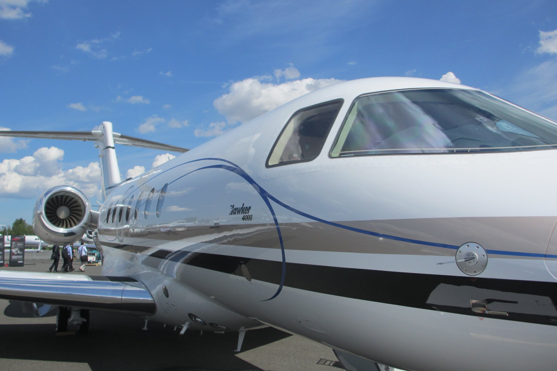 Hawker 4000 – Front fuselage and cockpit in Madrid Hawker 4000 private jet's front-side fuselage, cockpit windows, and engine under a blue sky, ready for routes from Madrid.