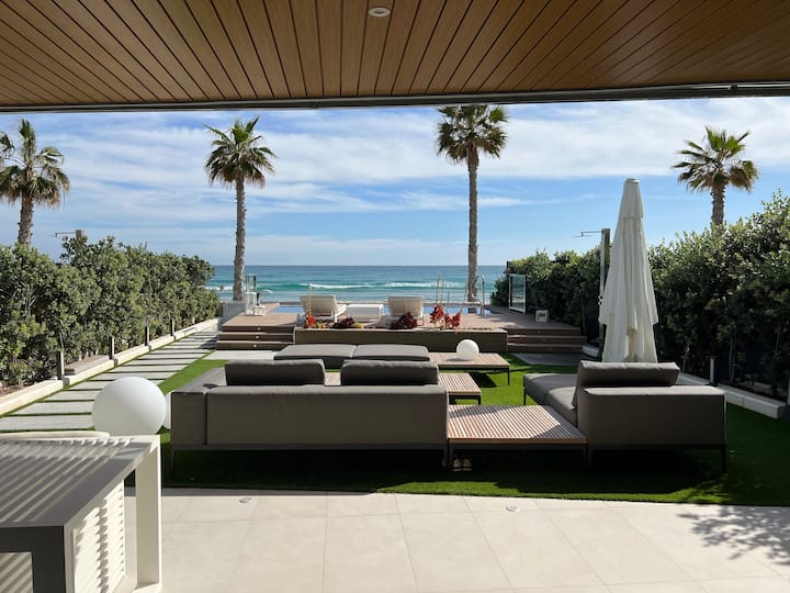 Bungalow Marta — Außenlounge mit Meerblick Der luxuriöse Außenbereich des Bungalow Marta bietet moderne Sofas, Kunstrasen und Palmen mit herrlichem Meerblick in Alicante.