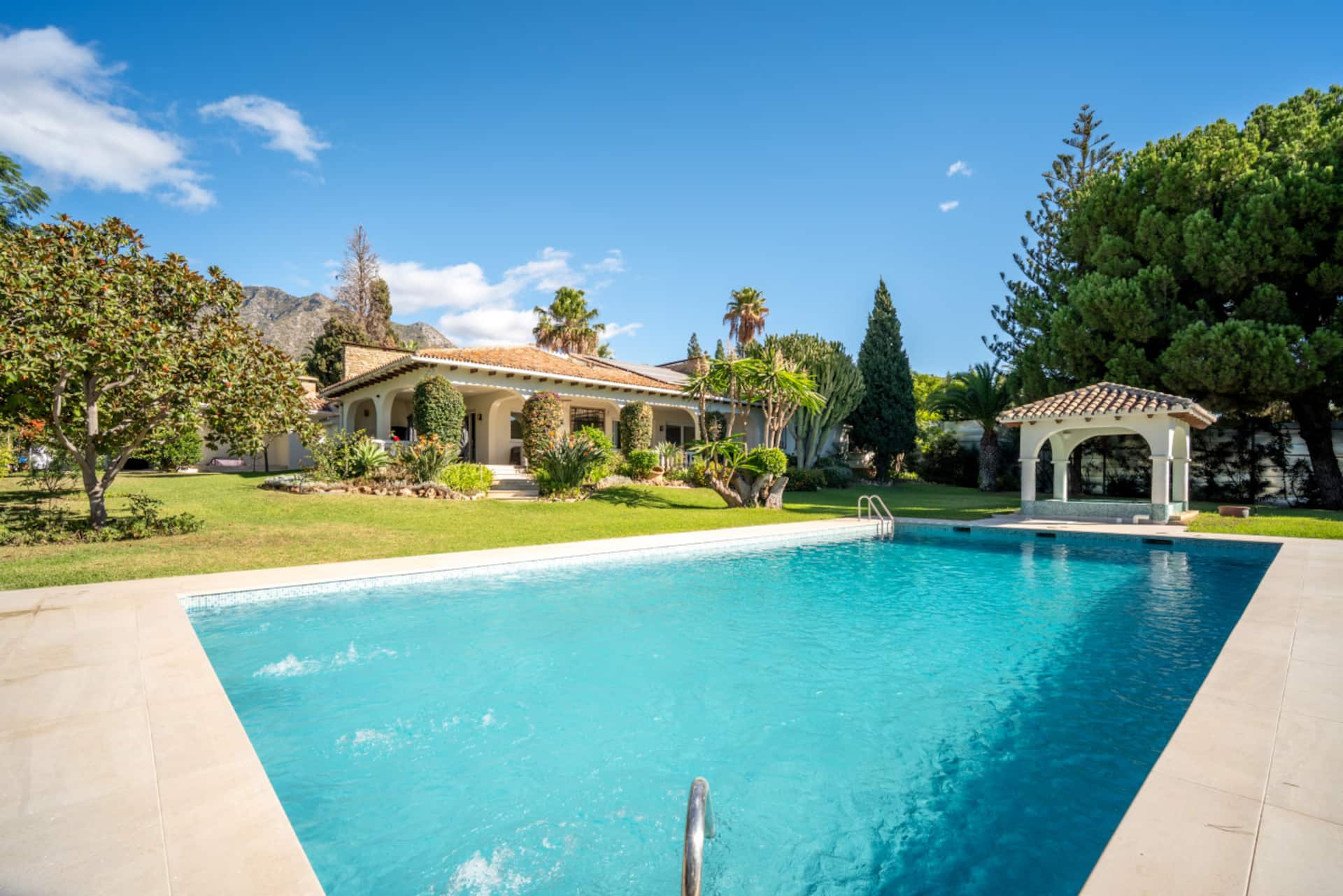 Villa La Concha — Pool- und Gartenaußenansicht Die Villa La Concha in Marbella, Spanien, zeigt einen großen Pool, üppige Gärten und das elegante Äußere der Villa unter klarem Himmel.