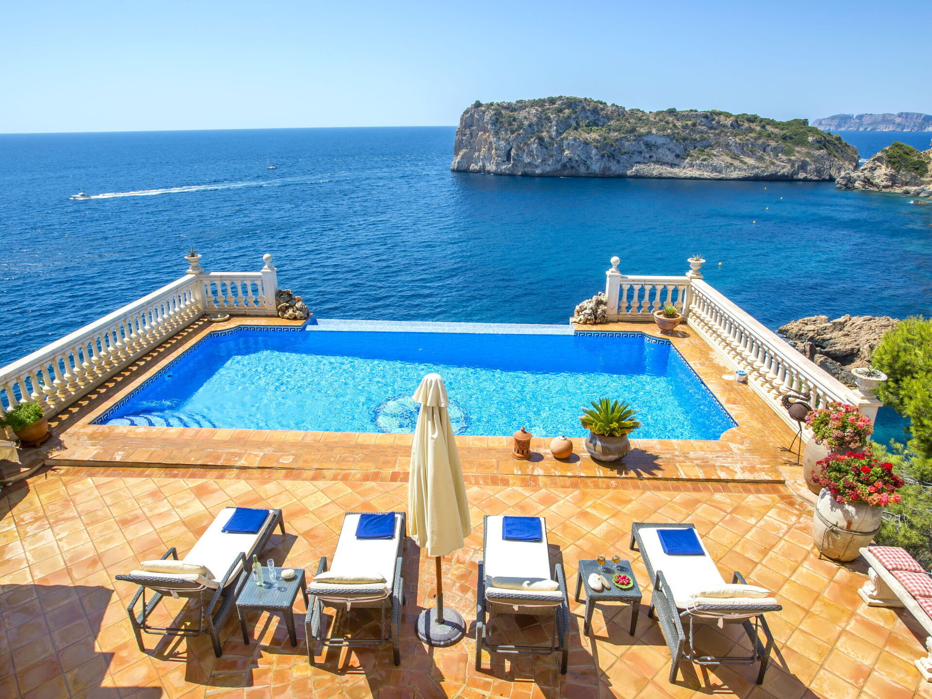 Villa Lauras Paradise — Infinity-Pool & Meerblick Der Infinity-Pool und die Terrakotta-Terrasse der Villa Lauras Paradise mit Sonnenliegen bieten einen atemberaubenden Blick auf das Mittelmeer und eine Felseninsel in Jávea, Valencia.