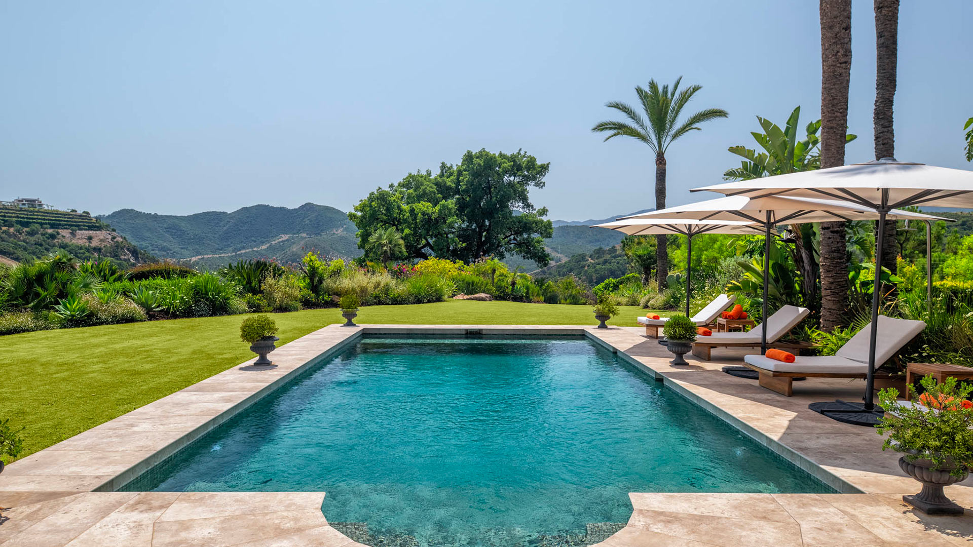 Villa Oasis des Collines' tranquil swimming pool area with sun loungers, lush gardens, and distant Marbella mountains.