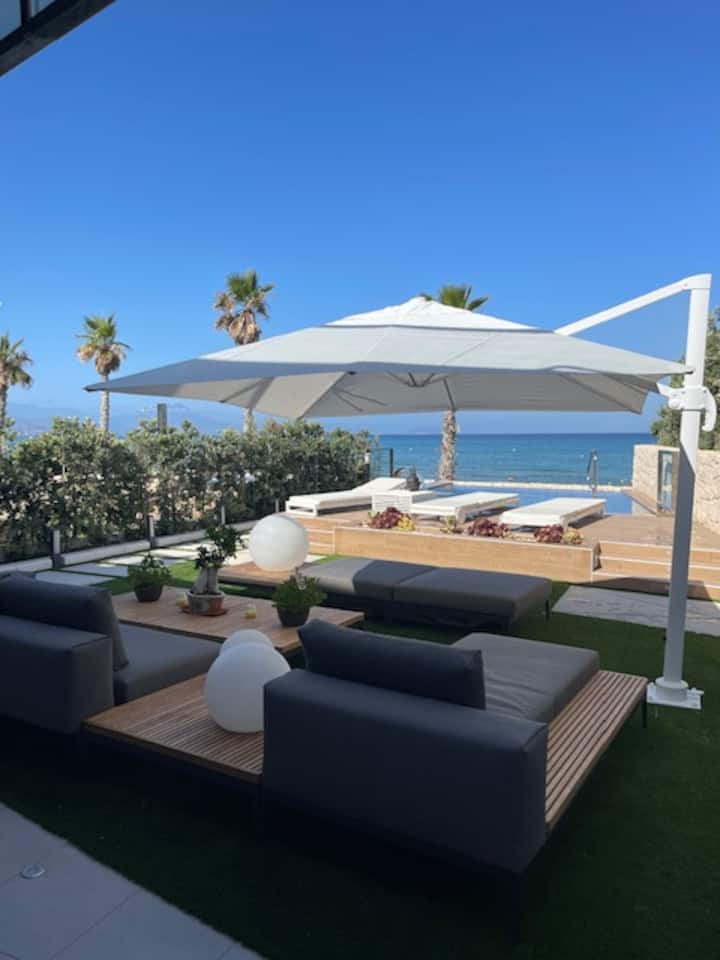 VILLA SEAS THE DAY — Außenlounge mit Meerblick VILLA SEAS THE DAY Außenlounge mit modernen Sitzgelegenheiten, großem Sonnenschirm, Infinity-Pool und Meerblick in Alicante, Spanien.