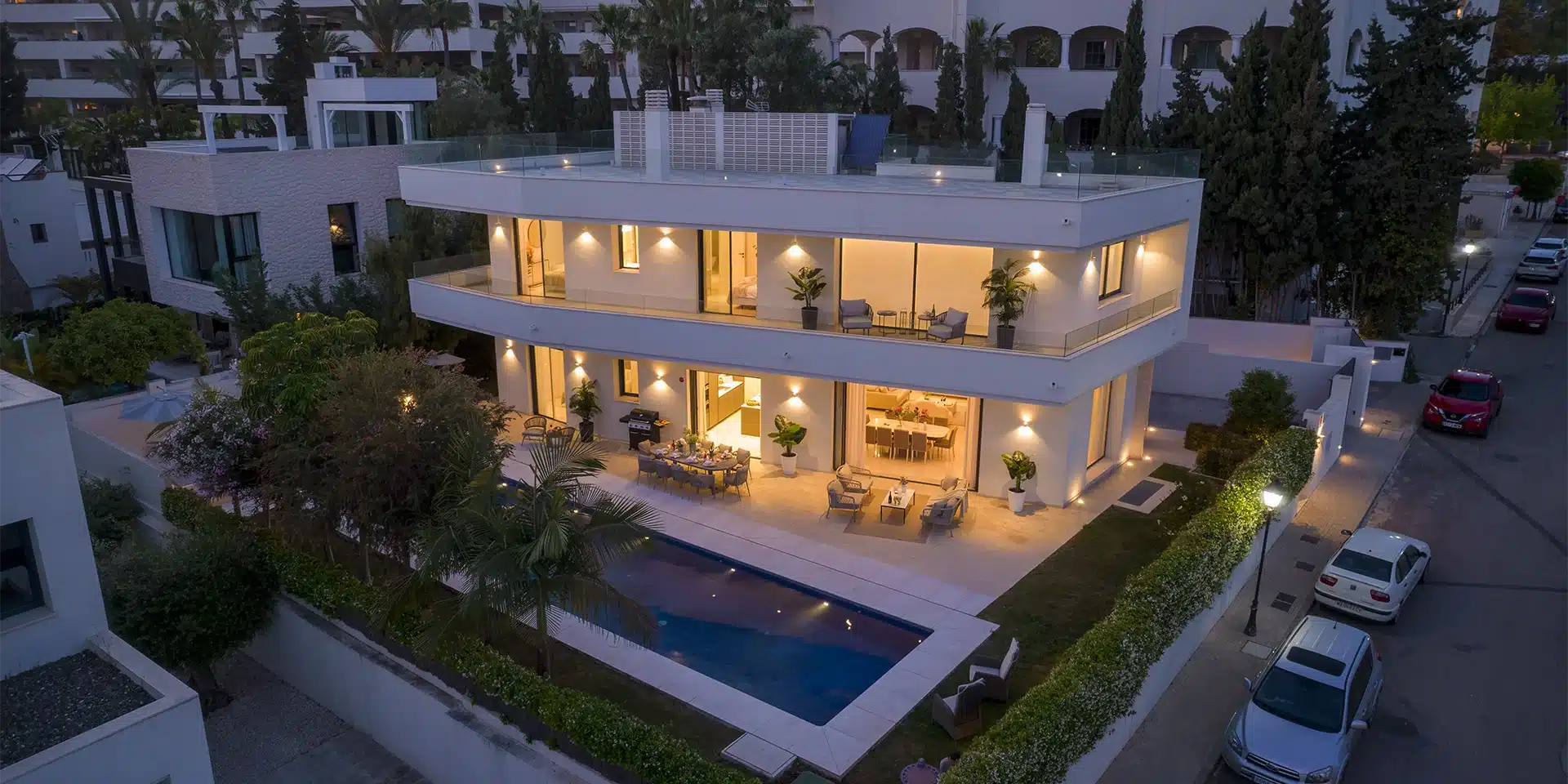 Villa Velazquez — Beleuchteter Außenbereich und Pool Die Villa Velazquez in Marbella, Spanien, zeigt bei Dämmerung ihr beleuchtetes, modernes Äußeres, den privaten beheizten Pool und elegante Außenterrassen.