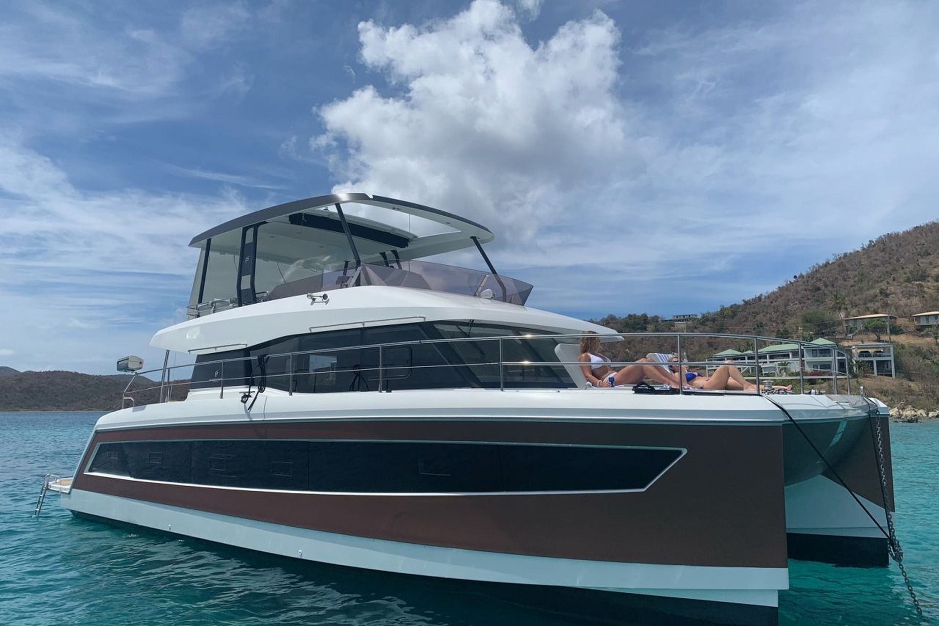 Der Katamaran Fountaine Pajot MY 44 ankert in klarem Wasser vor Mallorca, mit zwei Frauen, die auf seinem Vorderdeck sonnenbaden.
