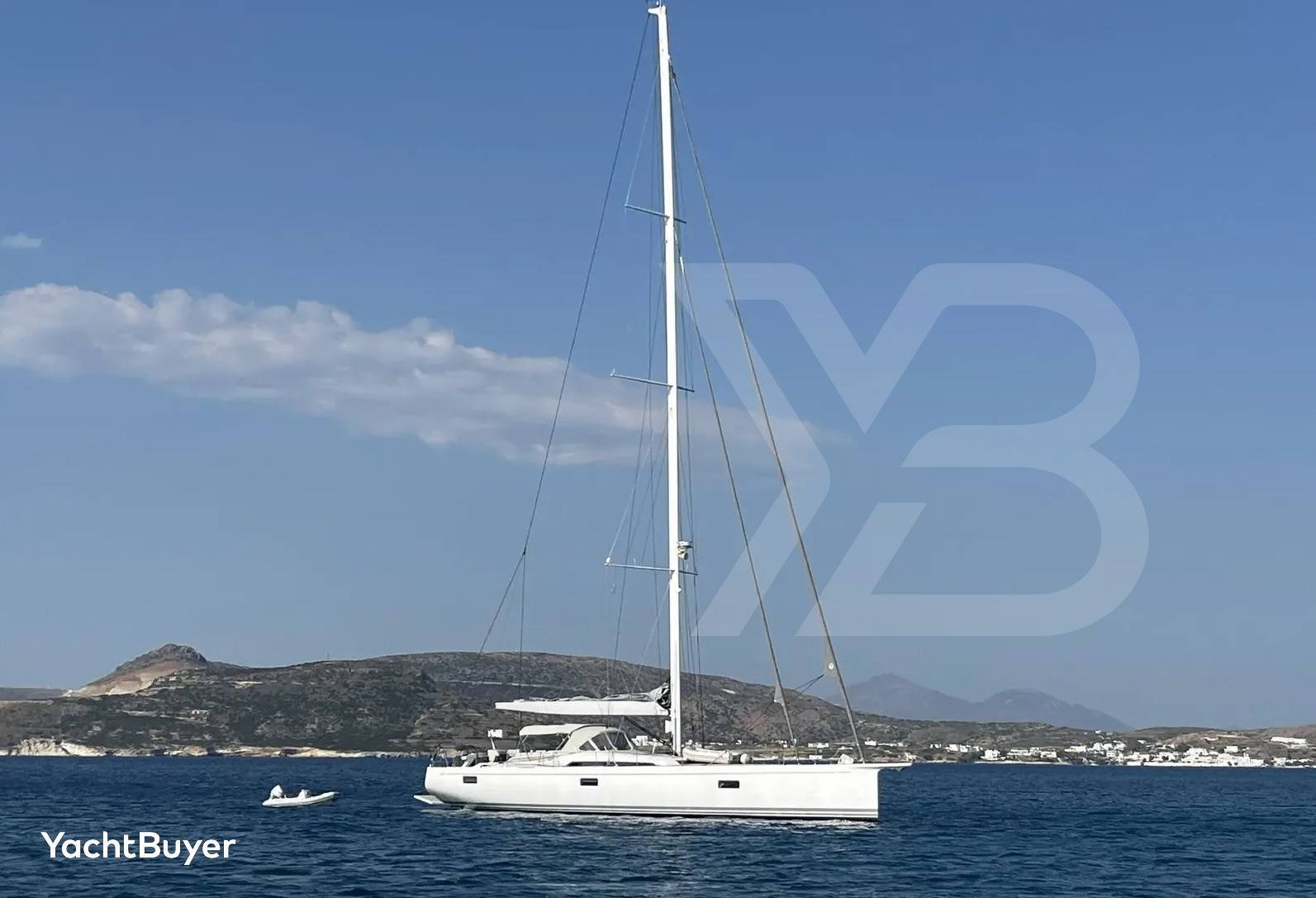 Die Nautor Swan 78 Segelyacht ist von der Seite zu sehen, elegant auf dem klaren blauen Mittelmeer vor einer hügeligen Küste.