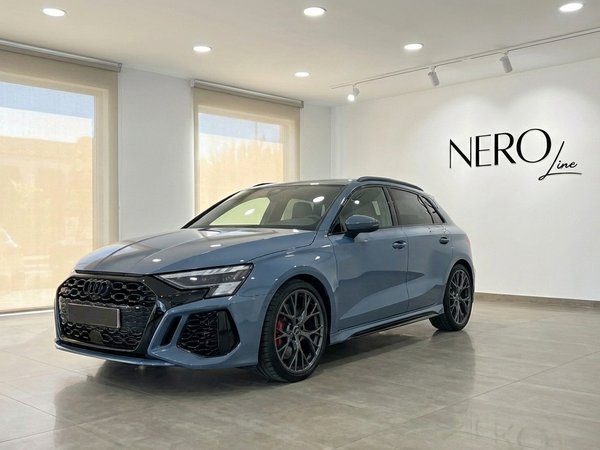 Audi RS3 — Luxury sedan in Alicante showroom A sleek blue-gray Audi RS3 luxury sedan is showcased from a front three-quarter angle inside a bright showroom in Alicante.