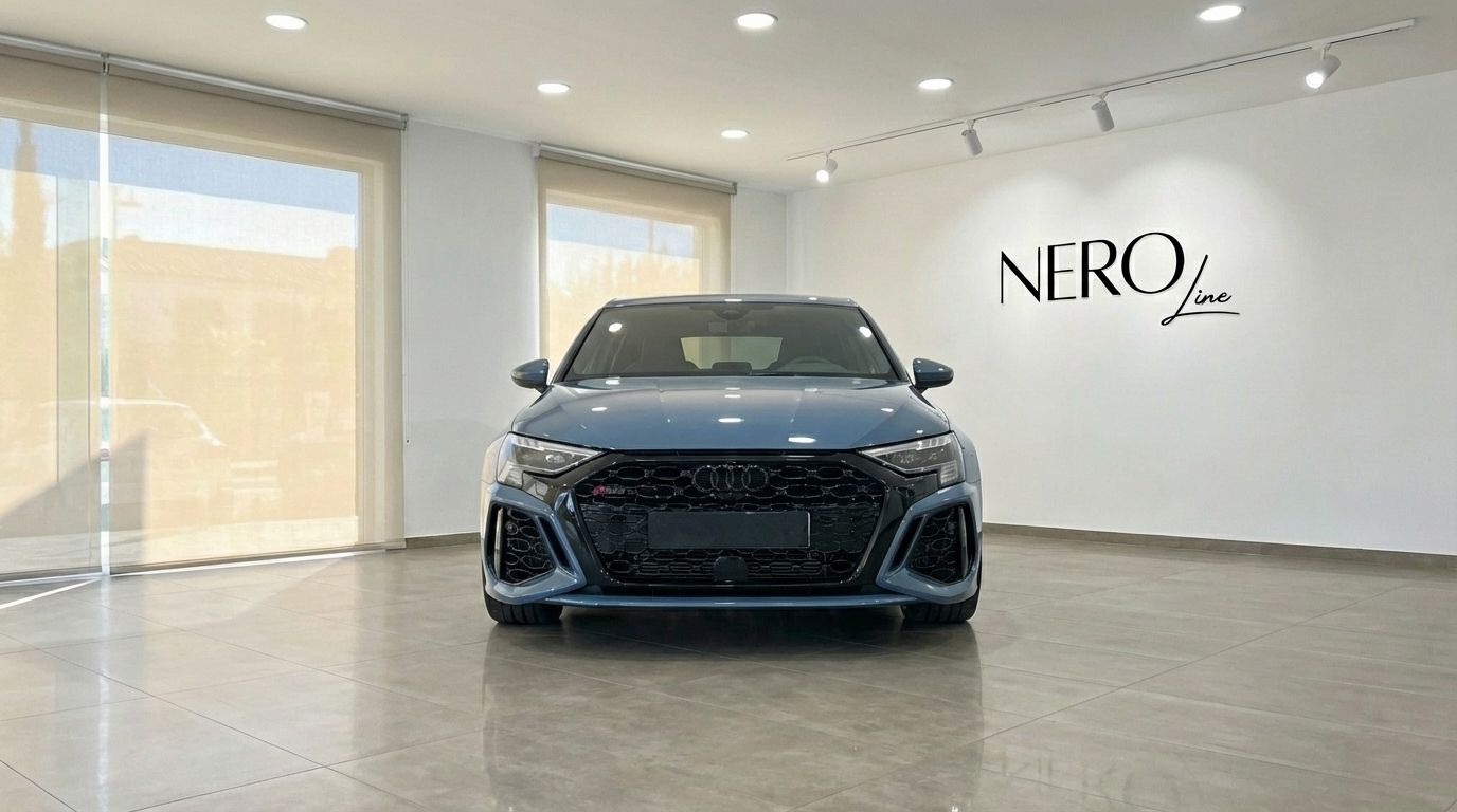 A blue-gray Audi RS3 2025 is prominently displayed in a showroom in Alicante, facing directly forward.