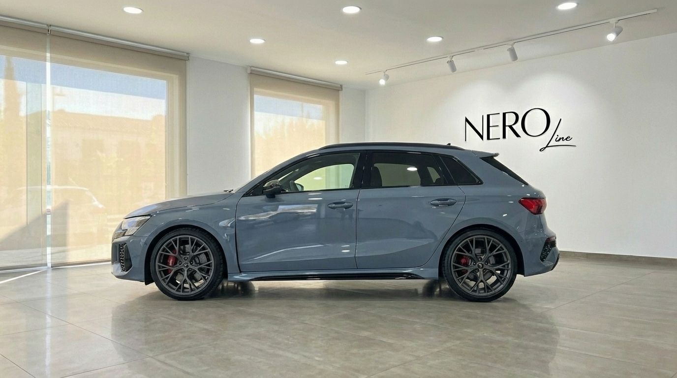 The sleek blue gray Audi RS3 is showcased from its side profile inside a modern showroom in Alicante, highlighting its sporty design.