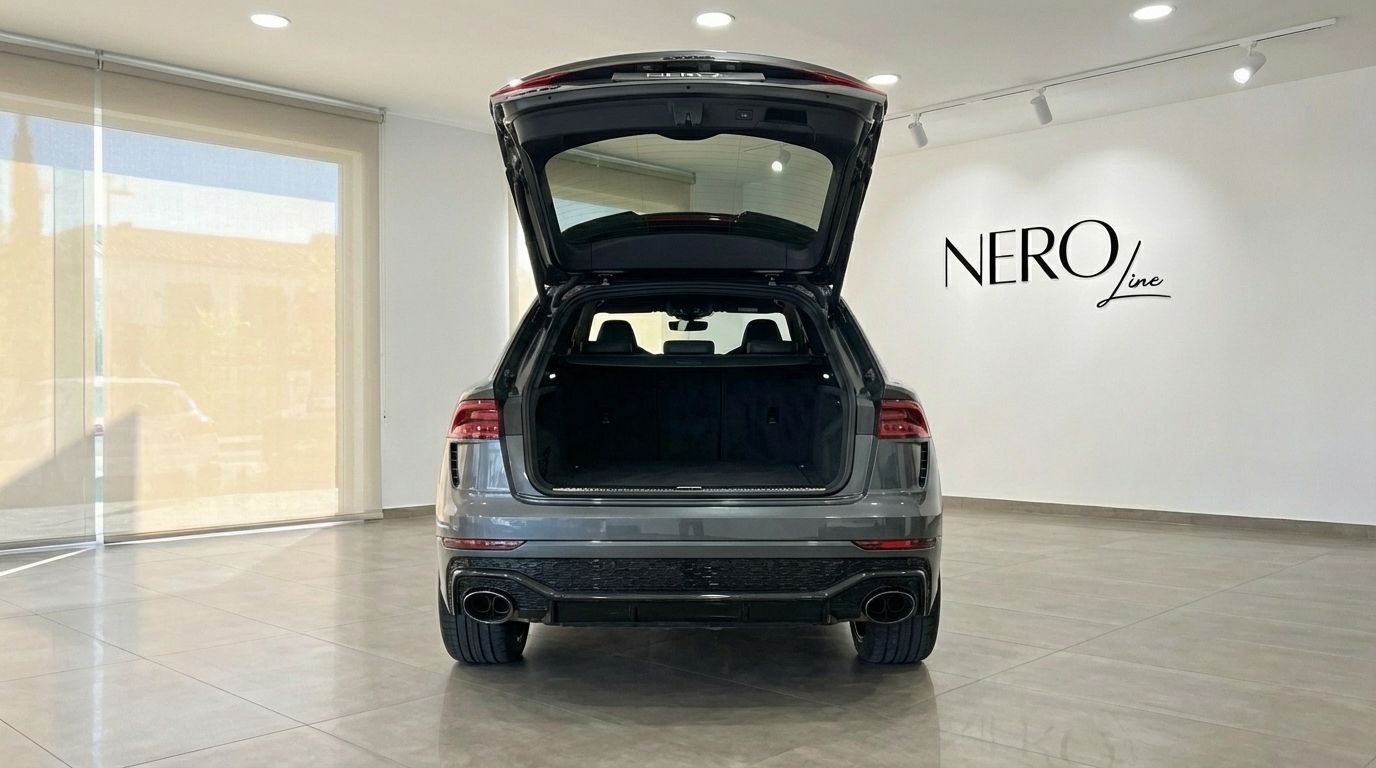 The metallic gray Audi RS Q8 is seen from the rear with its trunk open, showcasing its spacious cargo area in a showroom in Alicante.