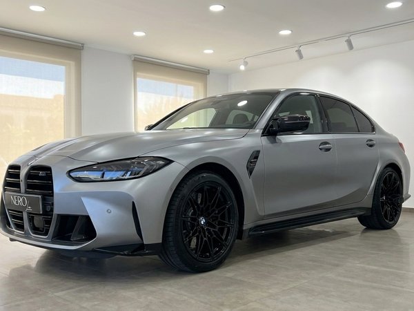 BMW M3 Competition xDrive — Vue avant Marbella La BMW M3 Competition xDrive gris pur mat givré est exposée de manière proéminente sous un angle trois-quarts avant dans un showroom de Marbella.