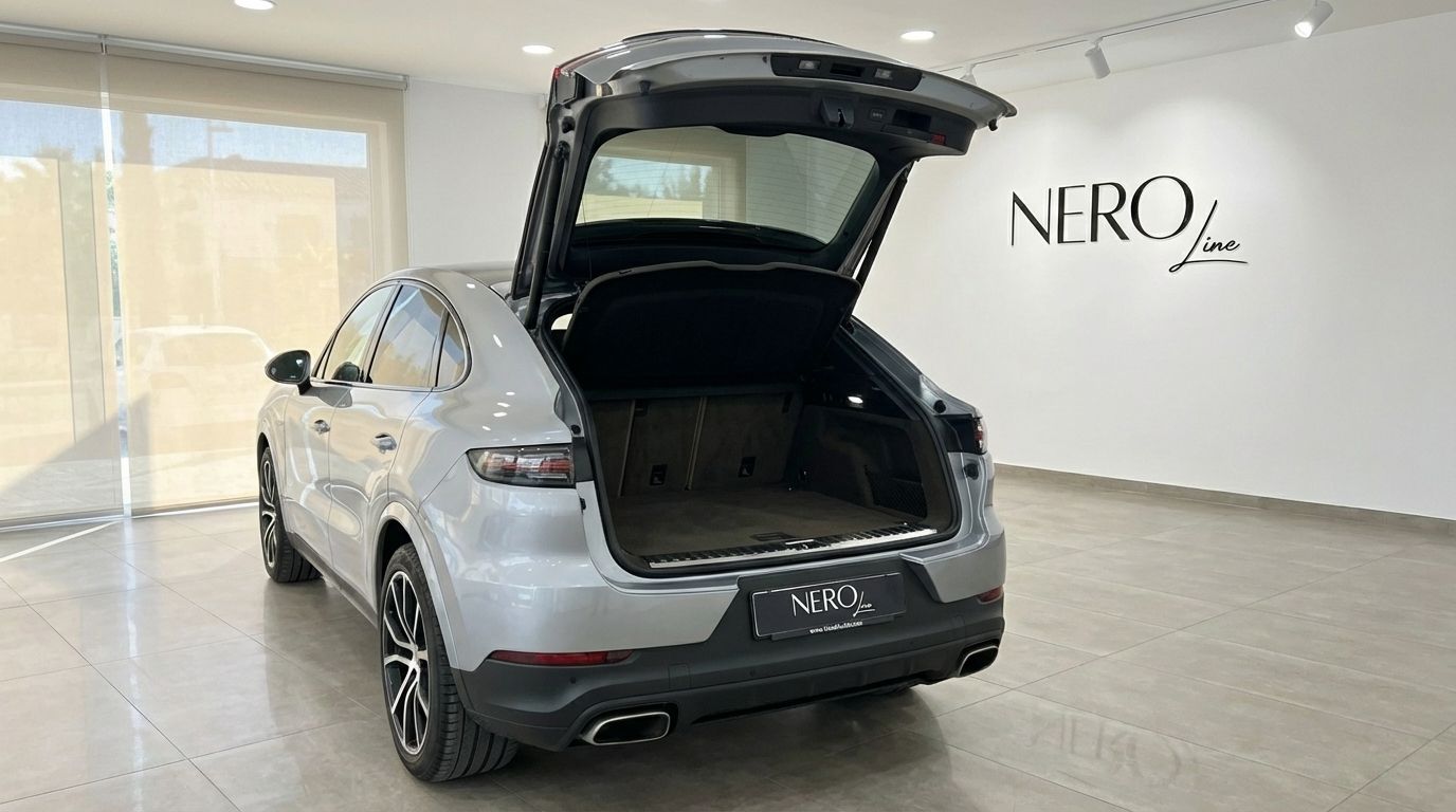 The silver metallic 2024 Porsche Cayenne Coupe is shown from the rear with its trunk open in a Marbella showroom.