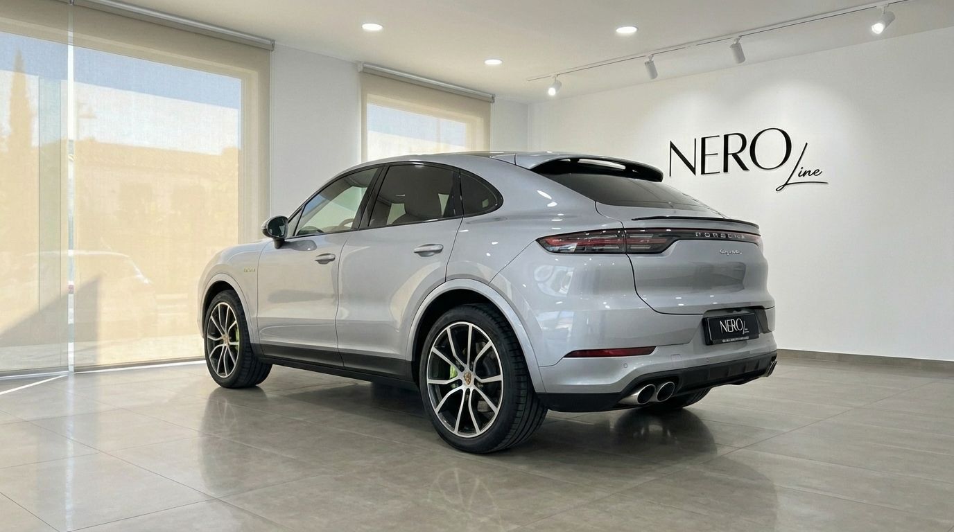 The silver 2024 Porsche Cayenne Coupe is showcased from a rear three-quarter angle inside a modern showroom in Marbella.