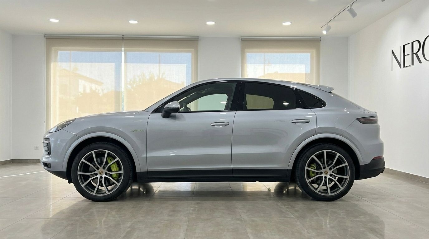 A silver metallic 2024 Porsche Cayenne Coupe is shown in a side profile view inside a showroom in Marbella.