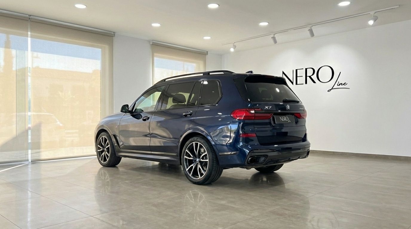 El SUV BMW X7 xDrive 2023 azul oscuro se muestra desde un ángulo trasero de tres cuartos en un concesionario en Alicante.