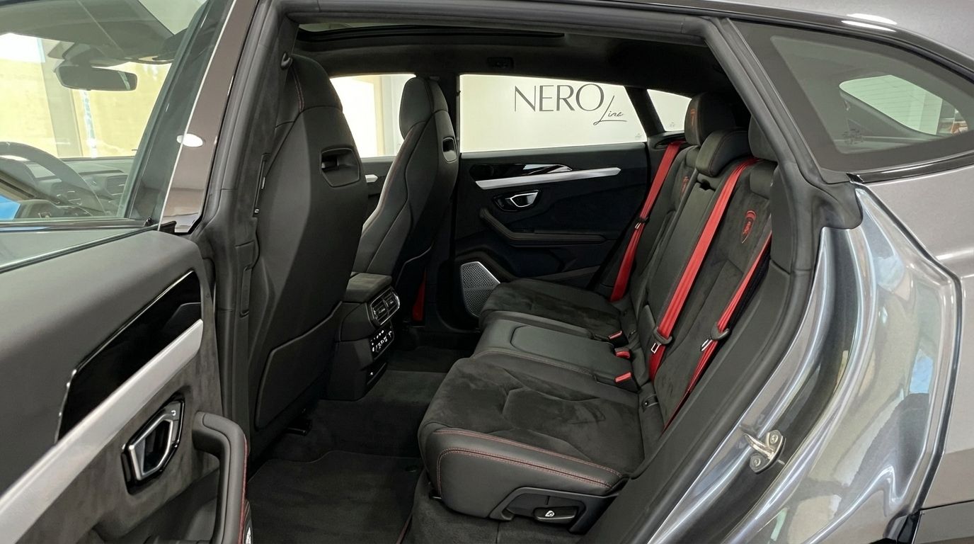 El lujoso interior trasero del Lamborghini Urus S en Madrid, mostrando asientos de cuero negro con costuras rojas y llamativos cinturones rojos.