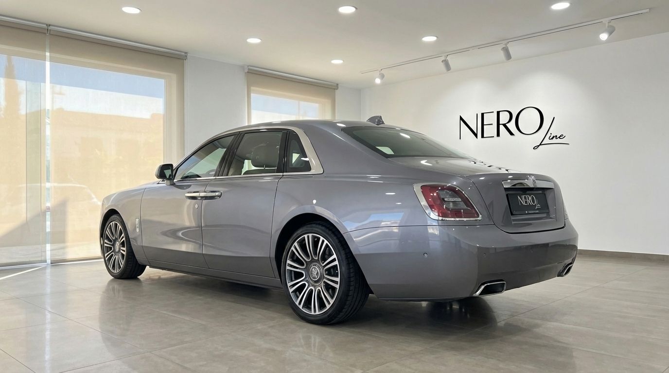 The metallic gray Rolls-Royce Ghost is elegantly displayed from a rear three-quarter angle inside a showroom in Valencia.