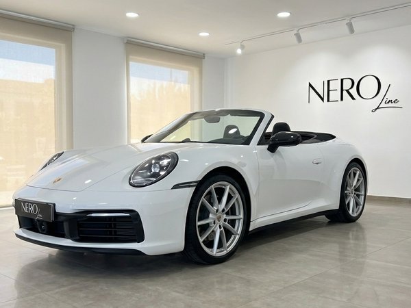 Porsche 992 Carrera Cabrio — Showroom view Mallorca The white Porsche 992 Carrera Cabrio is showcased with its top down, captured from a front three-quarter angle in a bright showroom in Mallorca.