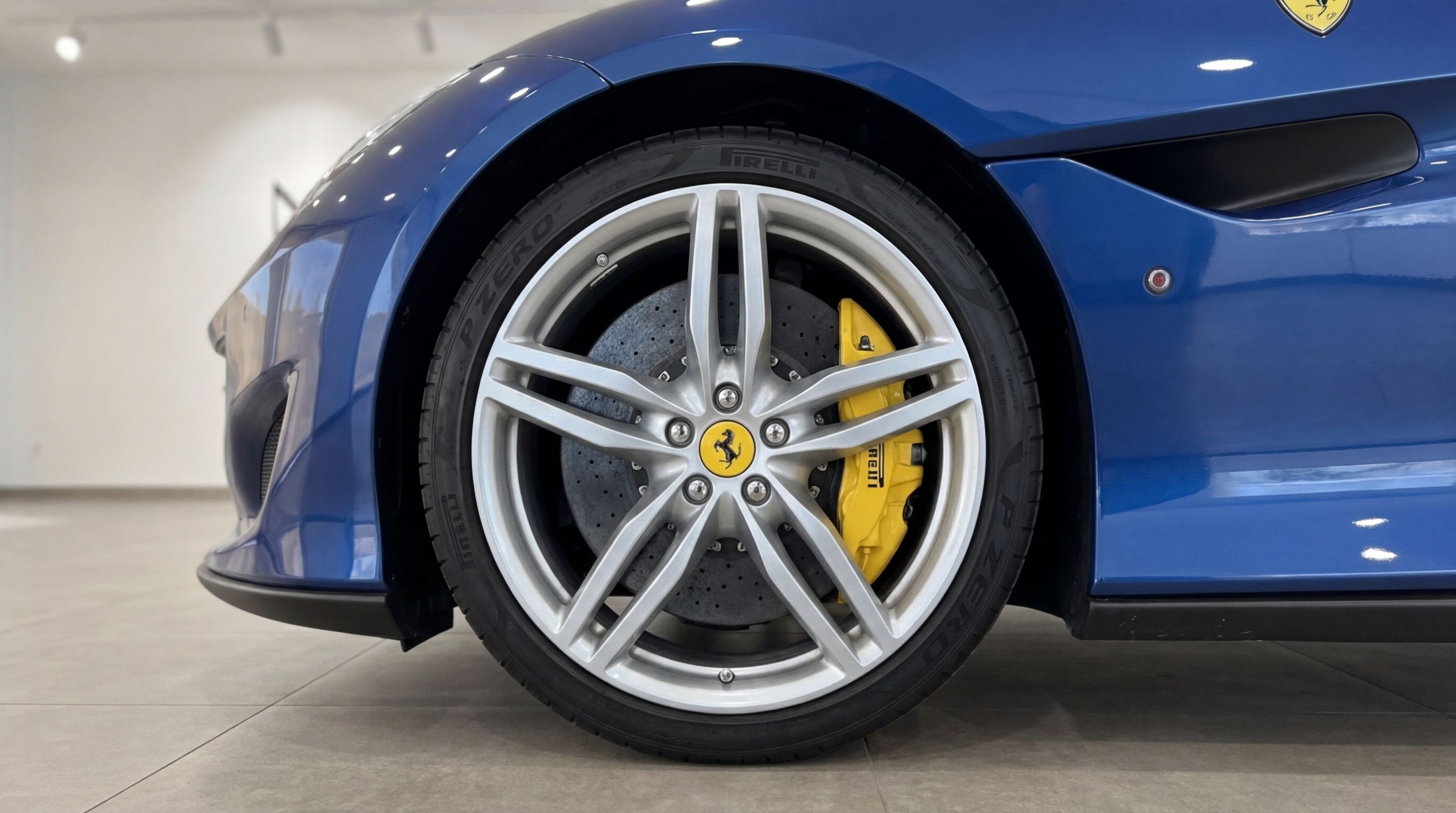 The metallic blue Ferrari Portofino in Malaga, showcasing its front wheel with a silver rim and distinctive yellow brake caliper.