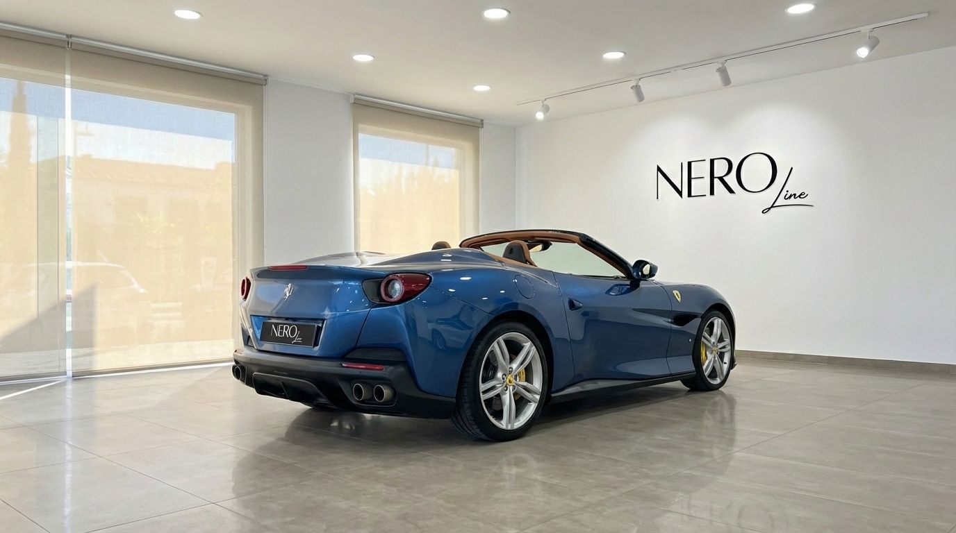 The metallic blue Ferrari Portofino convertible is showcased from a rear three-quarter angle in a Malaga showroom, with its roof down revealing the brown interior.
