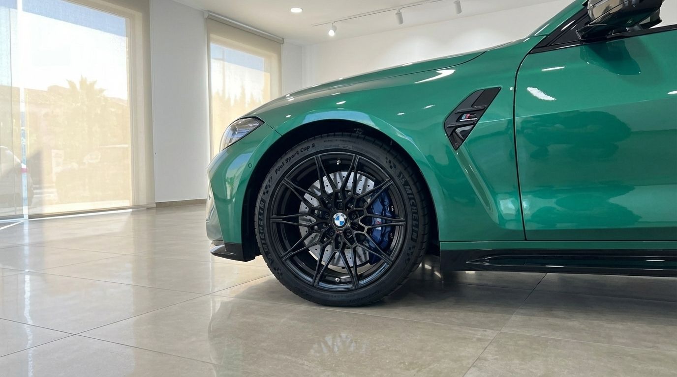 The emerald green BMW M4 Competition Convertible's front wheel with black rims and blue brake calipers is visible in an Alicante showroom.