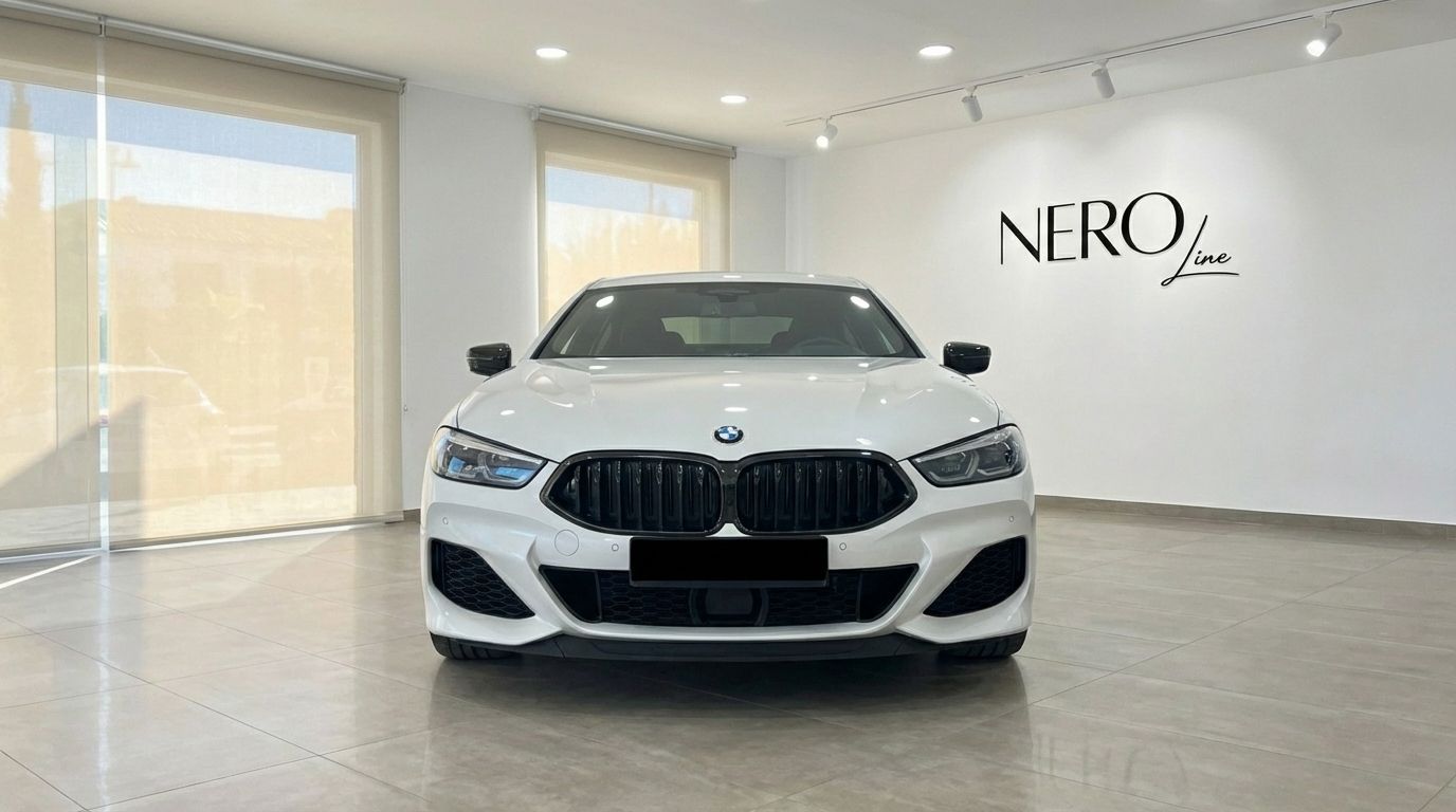 The white 2022 BMW M850i Grandcoupe is prominently displayed in a showroom, showcasing its sleek front grille and headlights in Barcelona.