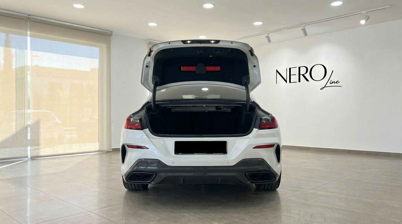 The white 2022 BMW M850i Grandcoupe is shown from the rear with its trunk open in a Barcelona showroom.