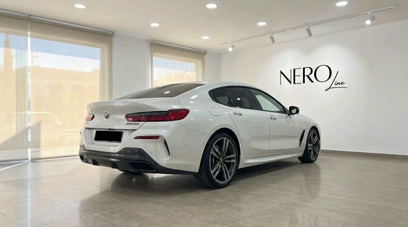 A white 2022 BMW M850i Grandcoupe is shown from a rear three-quarter angle in a showroom in Barcelona.
