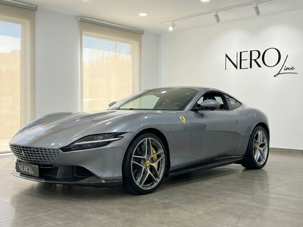 Ferrari Roma — Vista frontal tres cuartos, Madrid El Ferrari Roma 2022 gris metálico se exhibe desde un ángulo frontal tres cuartos en un luminoso showroom en Madrid.