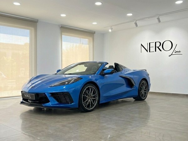 Chevrolet Corvette C8 Stingray — Exposición en Madrid El Chevrolet Corvette C8 Stingray convertible azul de 2024 se exhibe desde una vista frontal tres cuartos en un showroom en Madrid.