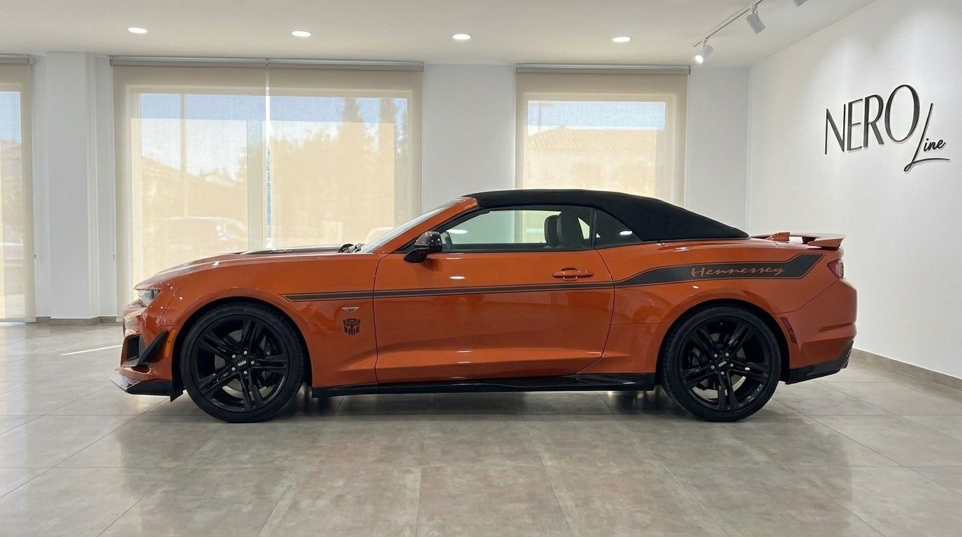 The orange Chevrolet Camaro Cabriolet 6.2, with a black soft top and racing stripes, is parked in a modern showroom in Alicante.