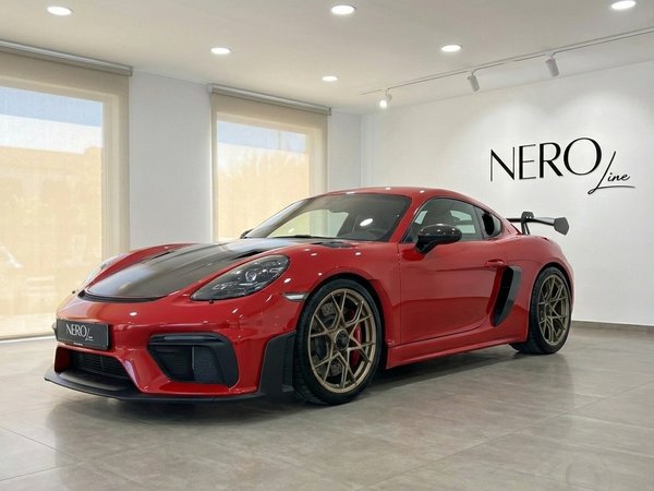 Porsche 718 Cayman GT4 RS – Alicante Showroom A striking red Porsche 718 Cayman GT4 RS 2026 is showcased in a modern Alicante showroom, featuring its aggressive front and gold wheels.