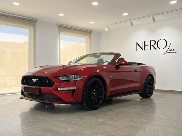 Ford Mustang GT Cabrio — Showroom in Alicante A racing red 2022 Ford Mustang GT Cabrio, seen from the front three-quarter angle with its top down, inside a modern showroom in Alicante.