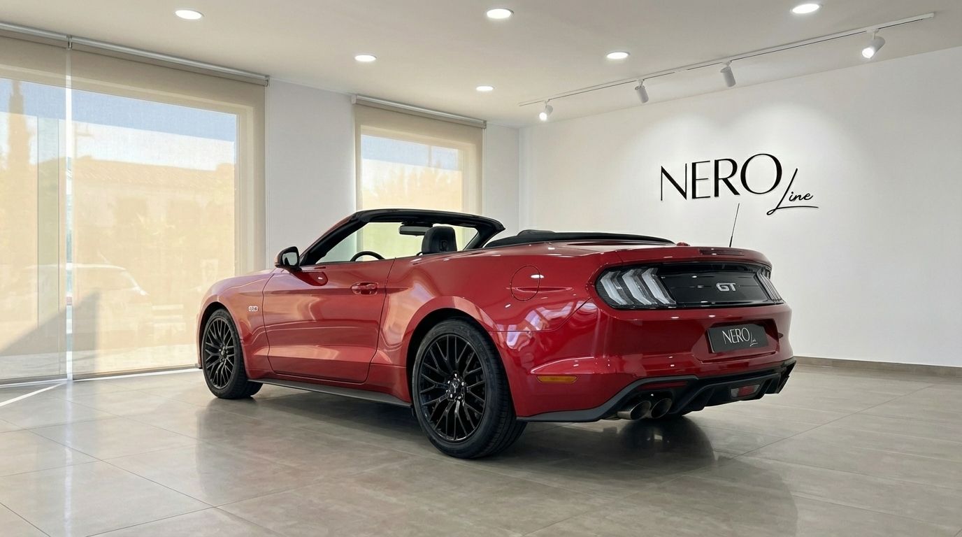 The red 2022 Ford Mustang GT Cabrio is shown from a rear three-quarter angle with its top down in a showroom in Alicante.