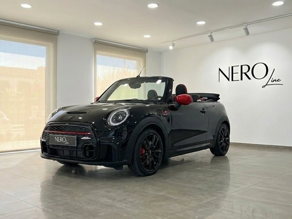 Mini John Cooper Works Cabrio — Showroom Barcelona The black Mini John Cooper Works Cabrio with red accents is showcased in a Barcelona showroom, viewed from the front three-quarter angle.