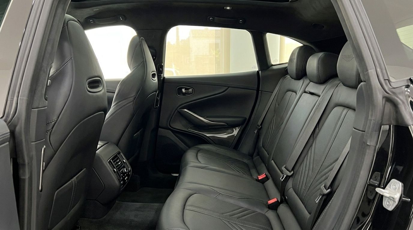 La imagen muestra los lujosos asientos traseros de cuero negro y el interior del Aston Martin DBX 707 en Ibiza.