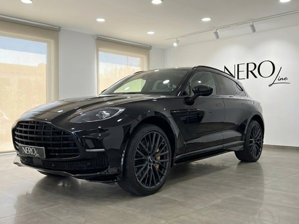 Aston Martin DBX — Vista frontal en showroom de Madrid El Aston Martin DBX negro de 2025 se exhibe desde un ángulo frontal tres cuartos en un luminoso concesionario en Madrid.
