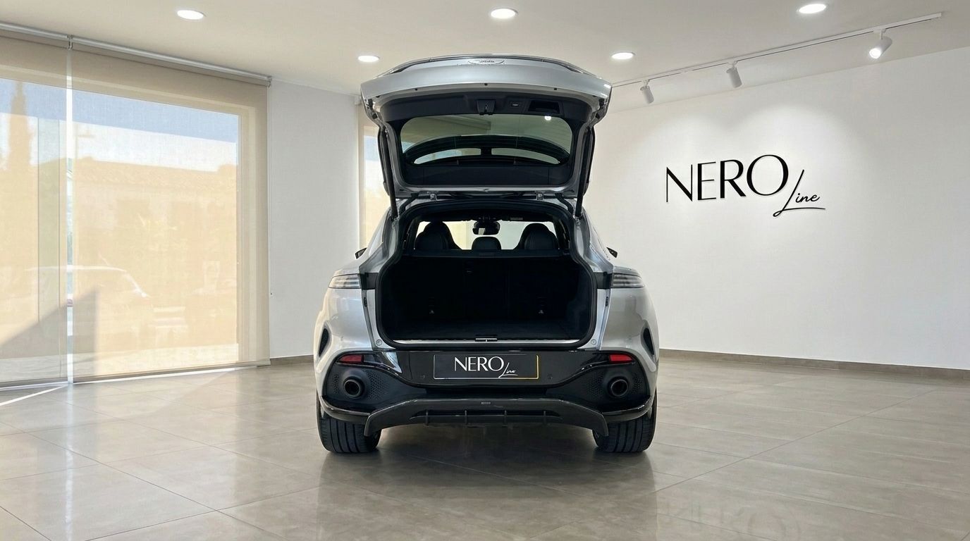 The rear view of a metallic silver Aston Martin DBX707 with its trunk open, parked in a showroom in Madrid.