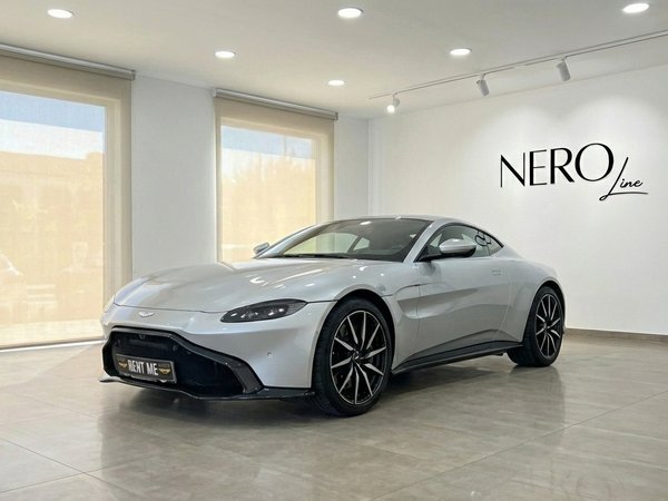Aston Martin Vantage V8 — Showroom in Marbella A silver-grey 2019 Aston Martin Vantage V8 is showcased from a front three-quarter view in a bright Marbella showroom.