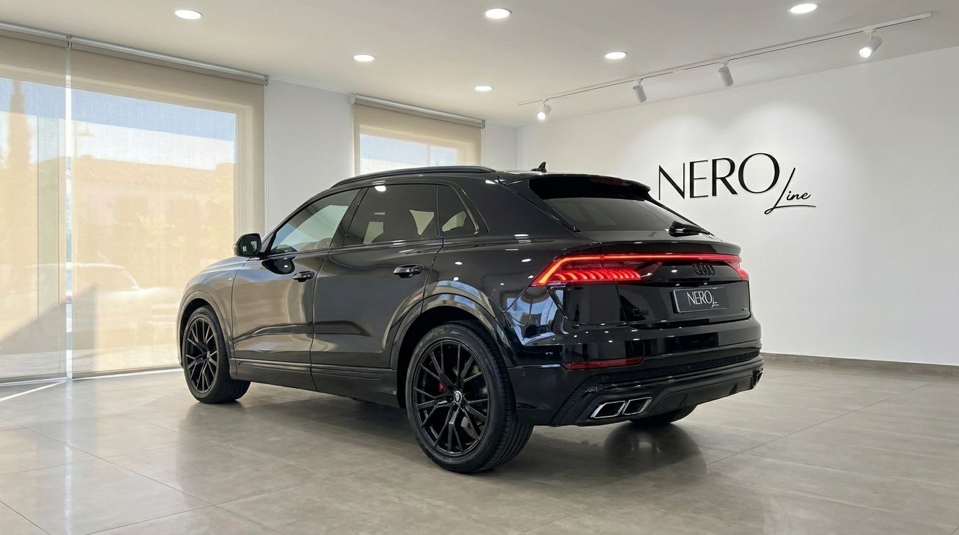 El Audi Q8 S-line negro de 2021 se exhibe desde un ángulo trasero tres cuartos en un luminoso concesionario en Marbella.