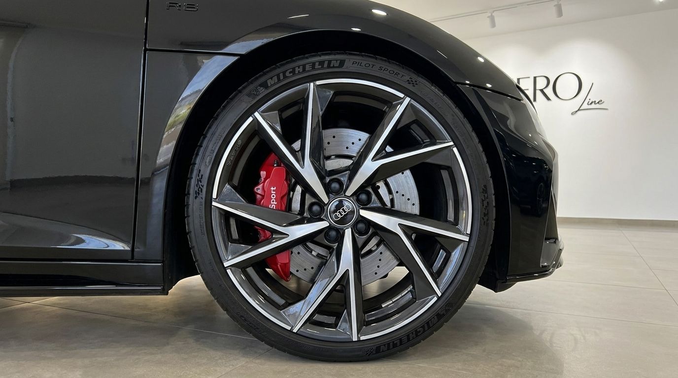 Primer plano de la rueda delantera del Audi R8 Spyder negro brillante con llantas plateadas de radios múltiples y pinzas de freno rojas en Marbella.