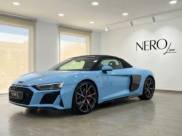 Audi R8 Spyder — Vista tres cuartos frontal, Madrid Un Audi R8 Spyder descapotable azul claro se exhibe desde una vista tres cuartos frontal dentro de un concesionario en Madrid.